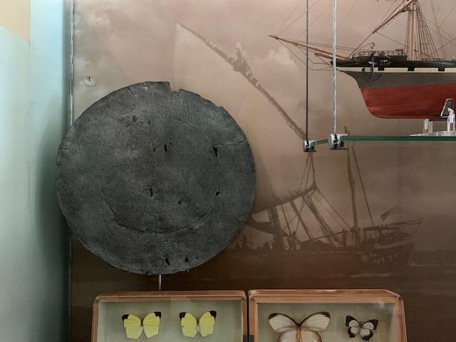 A flattened metal dish inscribed with text, featuring holes and a rough edge.