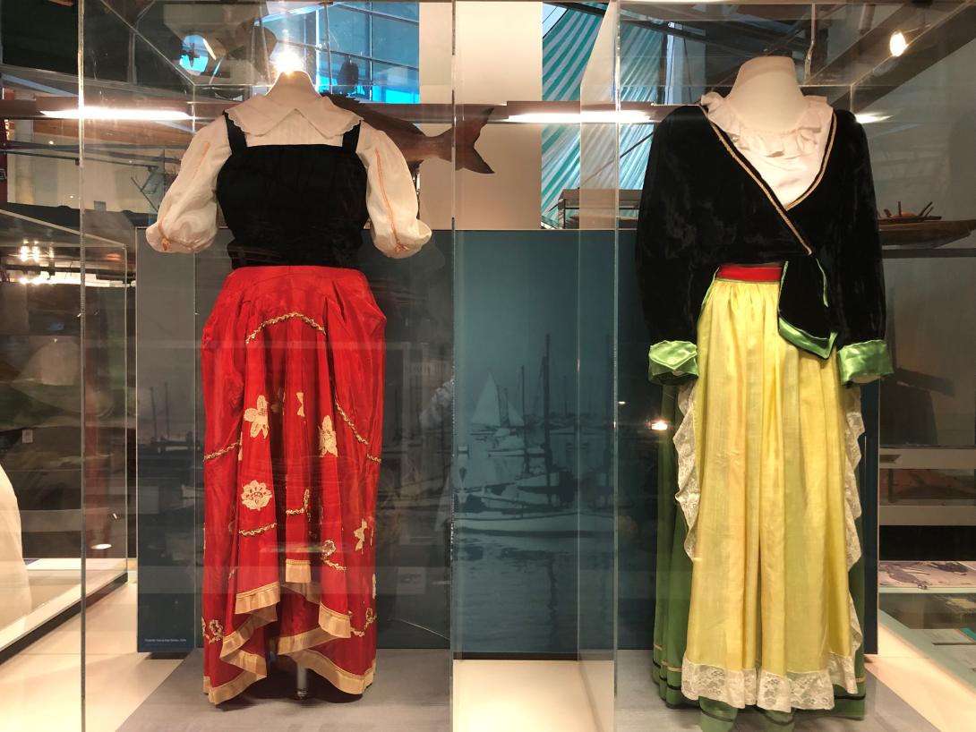 Two women's outfits on mannequins in a display case, one with a red skirt and the other with yellow.