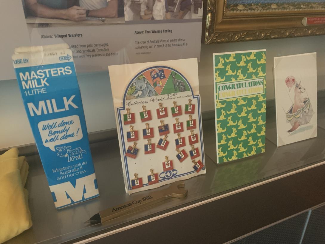 A display of a blue milk carton, commemorative lapel pins, novelty spanner pen, and two greeting cards.