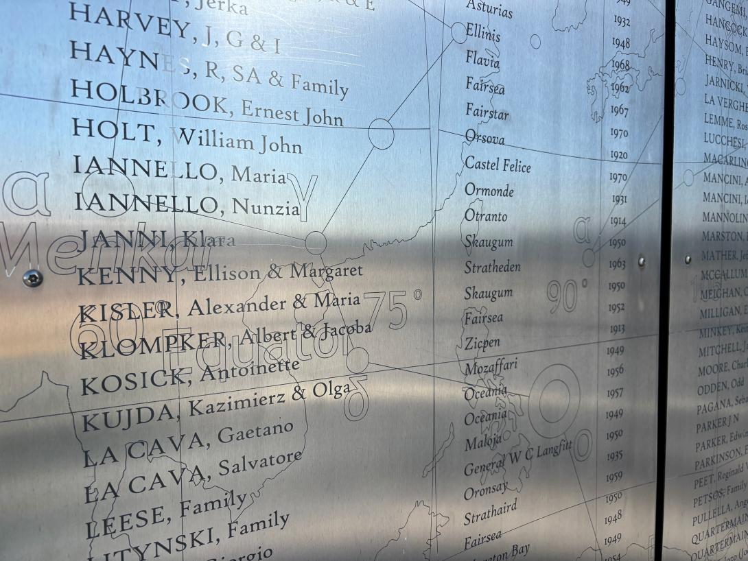 A close up of a silver wall inscribed with the names of passengers, the dates they arrived and the ship they sailed in on.names of