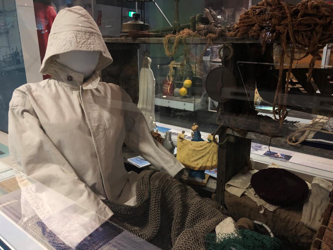 A mannequin wearing a white rain suit and hood sits in front of a display of fishing equipment.