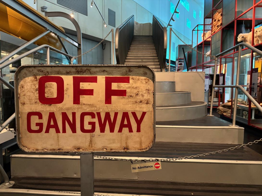 A vintage white sign with red lettering pictured at the based of a roped-off gangway.