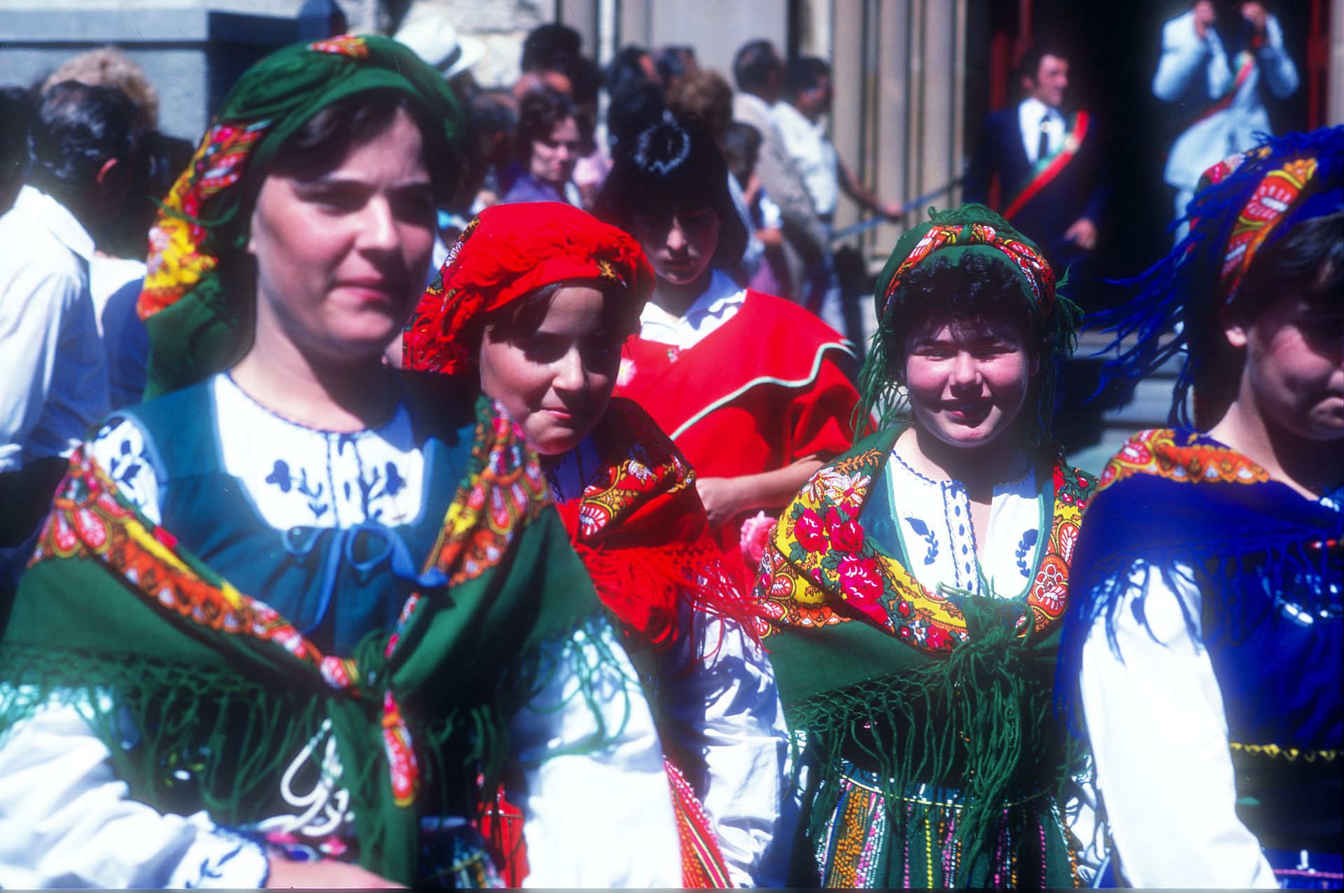A woman and 4 girls wear colourful traditional Italian dress, with bright scarves and shawls in reds, greens and blues.