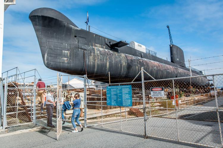 Beside the Museum, the big submarine sits behind a fence with three historic loading cranes around it.