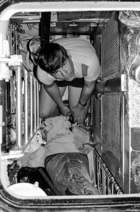 A young man looks up at the camera from the bottom of a room that is no larger than a wardrobe.