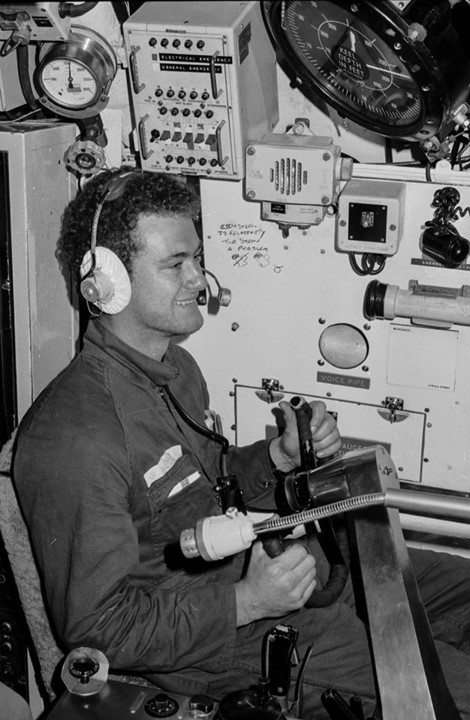 A grinning crewmember takes the submarine's steering wheel.