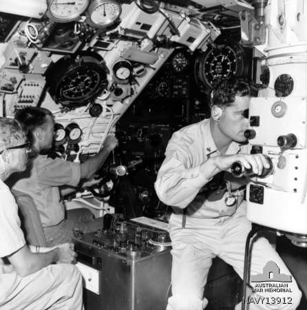 A crew member in white peers through a periscope.