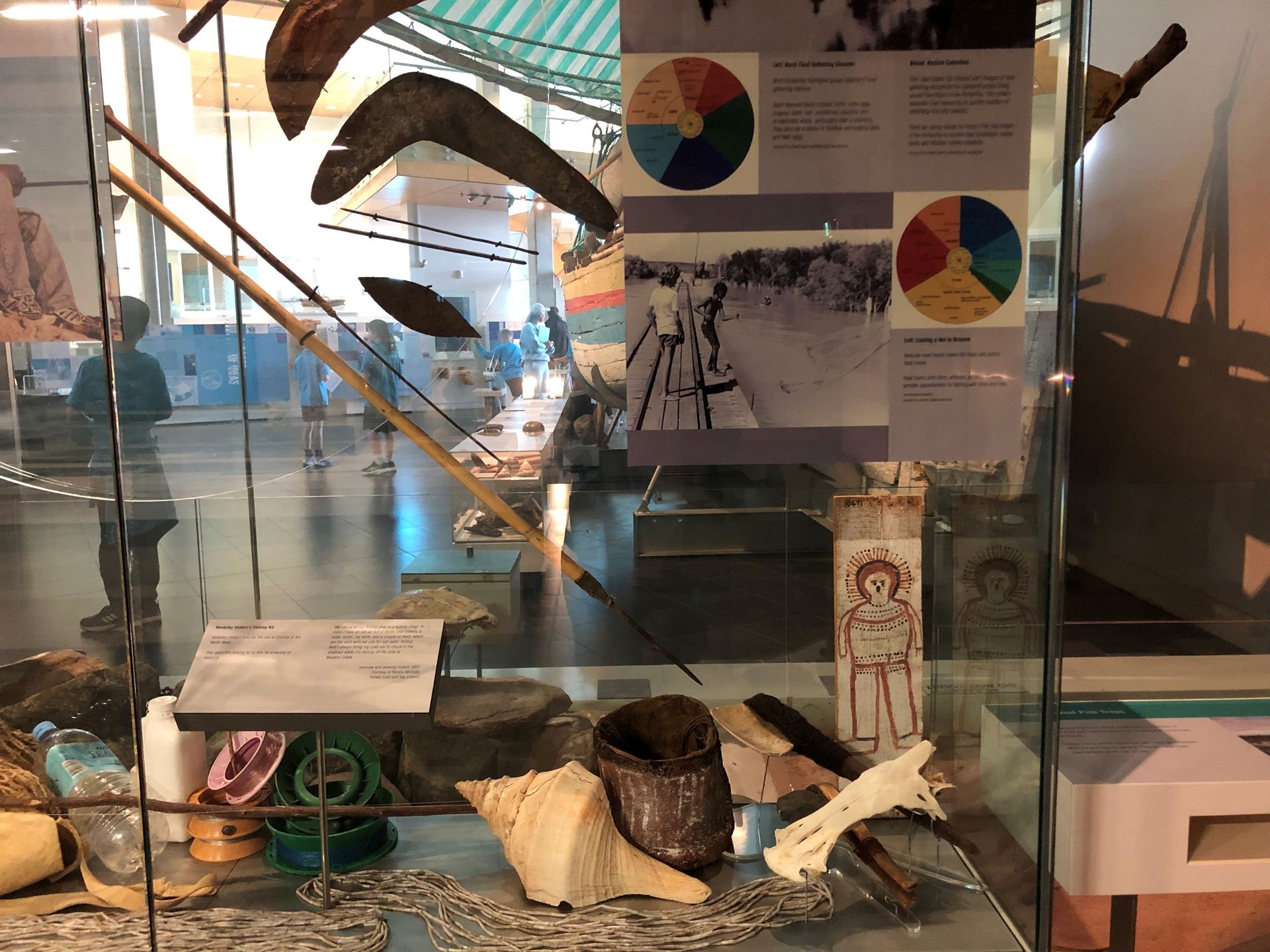 A glass display case filled with spears, boomerangs, shells and other material related to fishing.