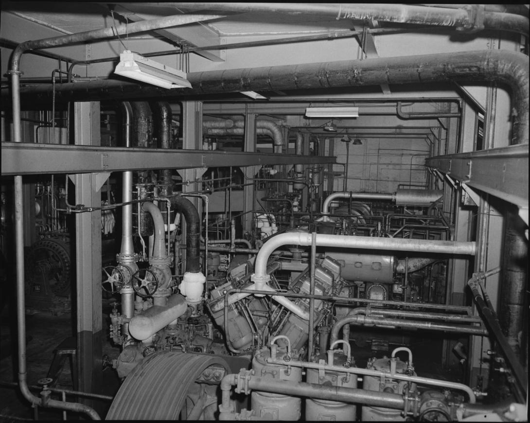 Many pipes and a lot of machinery fill a concrete room.