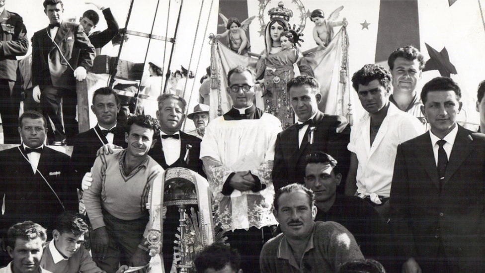 A Catholic priest and statue of Mary surrounded by parade participants.