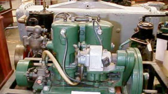 A marine engine on display, painted green with two cylinders vertical in the centre.