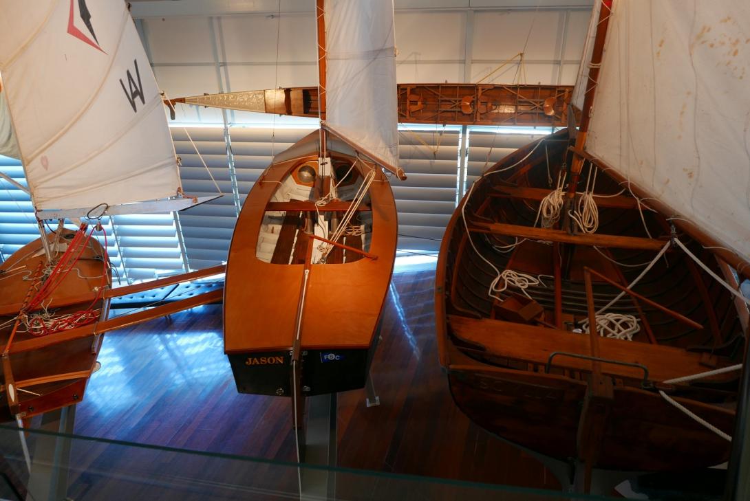 Three small wooden sailing craft, suspended in a row beside the Swan River Gallery walkway.