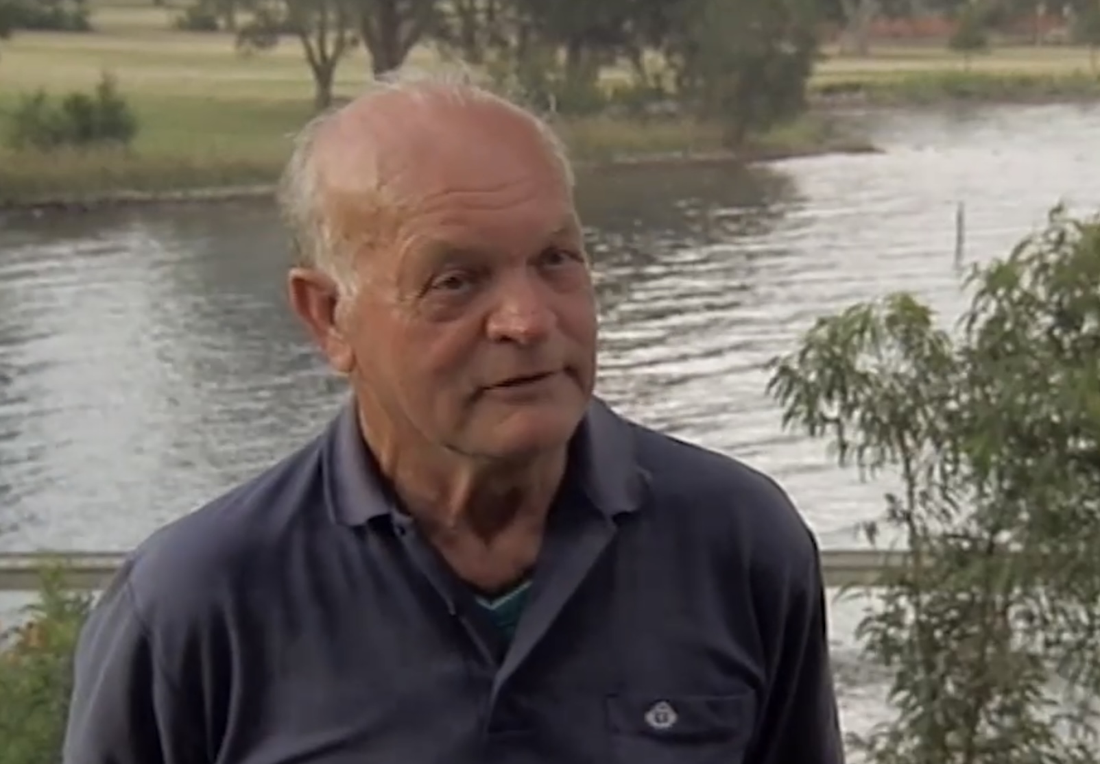 A man chats to the camera in front of a flowing river .
