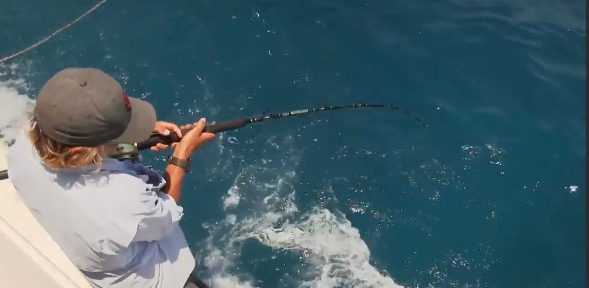 A person standing on a boat with a fishing rod has caught something, the rod is sharply bent downward.