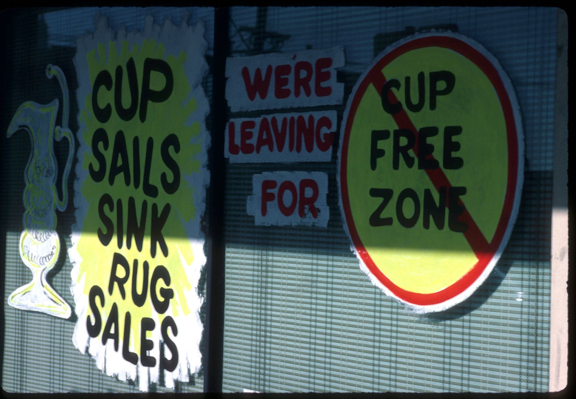 Anti-Australia Cup signs painted on a local shop window. Signs read "Cup sails (spelled S. A. I. L.) sink rug sales (S. A. L. E.)" Another reads, "Cup free zone."