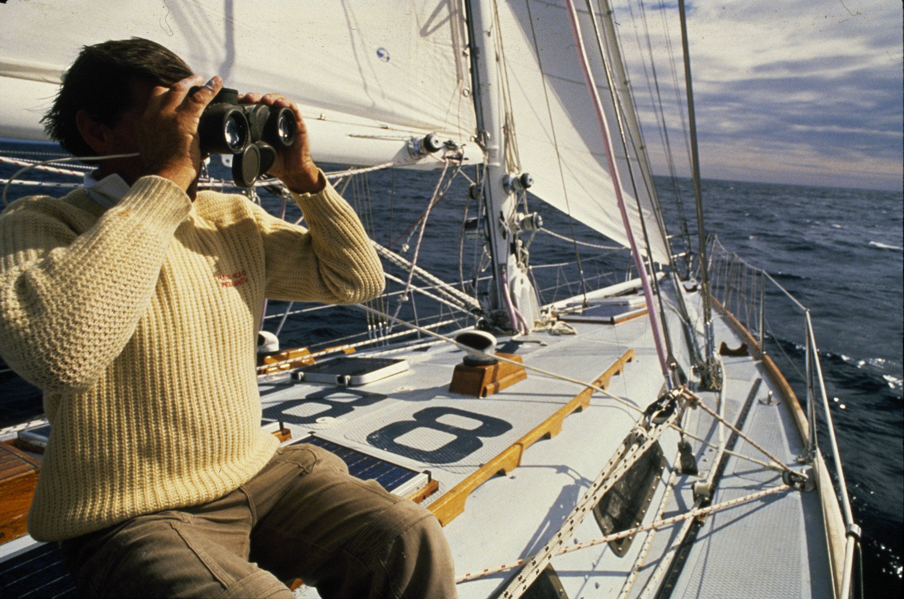 Jon Sanders sitting on the deck of the yacht, look at the distance through binoculars.
