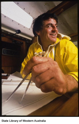 Jon in a bright yellow jacket smiling as he measures a distance on a sea chart.