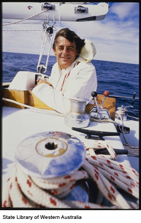 A close-up photo of Jon Sanders smiling with an arm resting on the boat. The ocean is calm behind him.