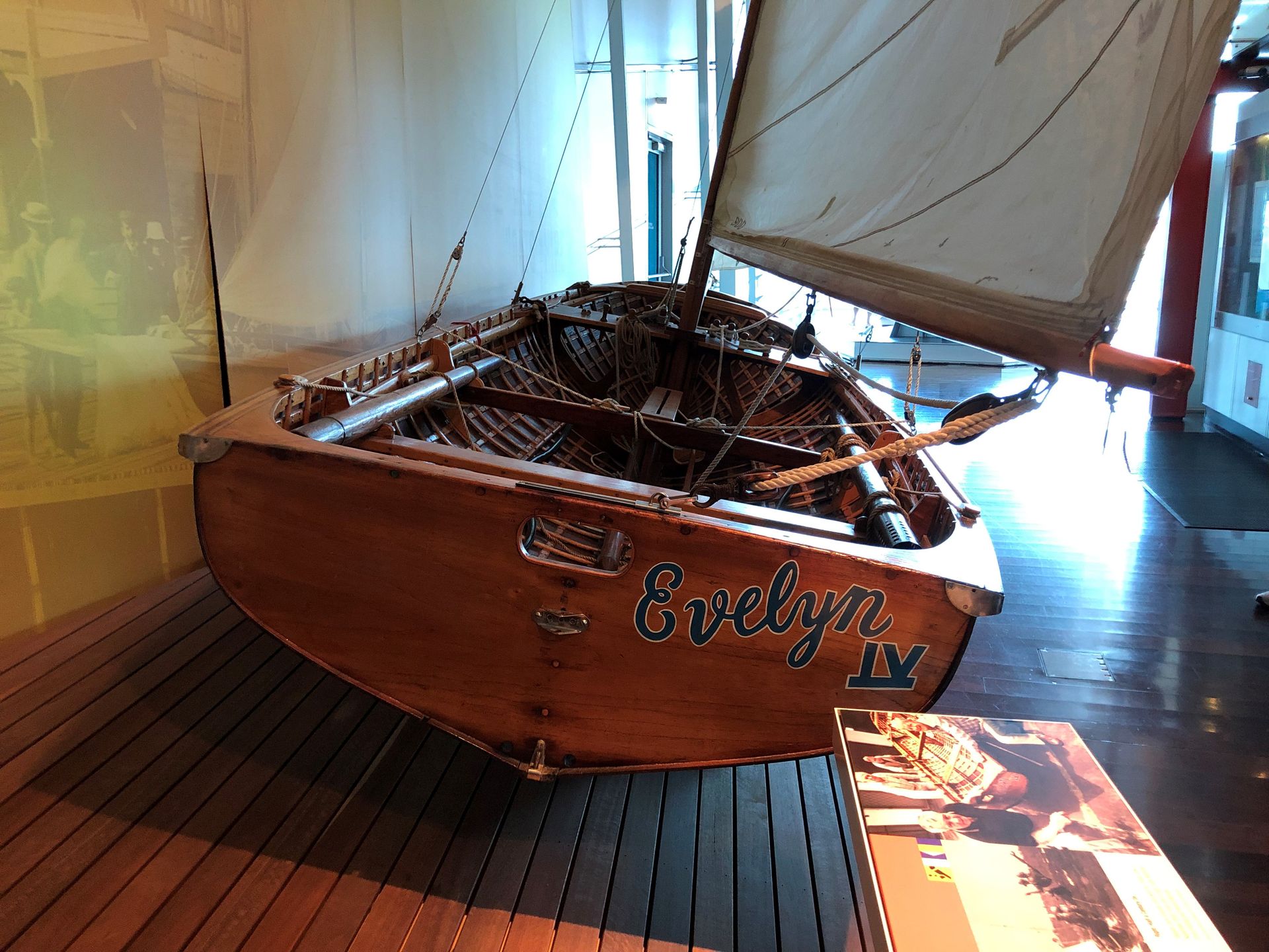 Against the Museum's wall mounted on a long wooden platform on the floor is a small wooden yacht with one sail.