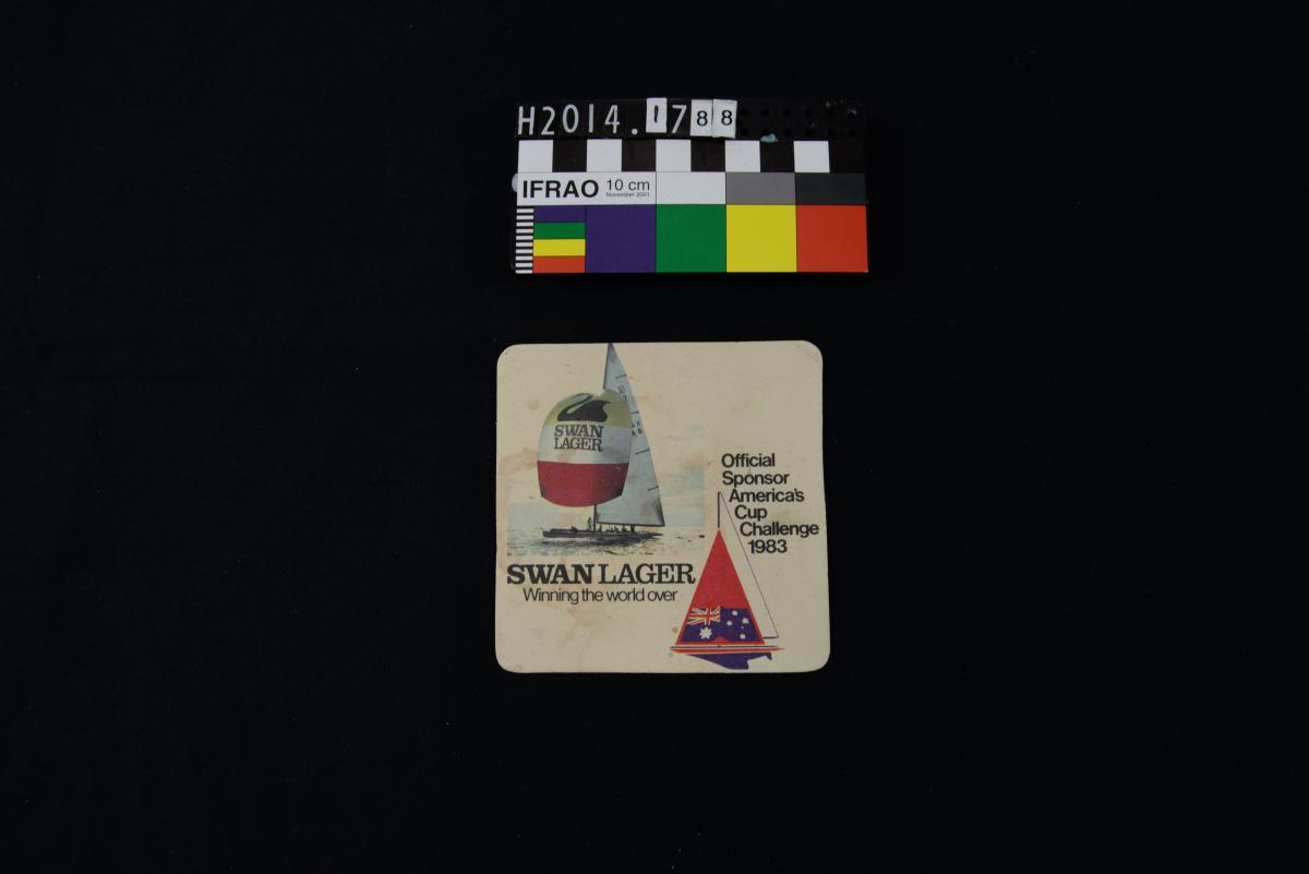 A white beer coaster, discoloured with age. A yacht is depicted. Text reads "Swan Lager: Winning the world over. Official sponsor, America's Cup Challenge 1983."
