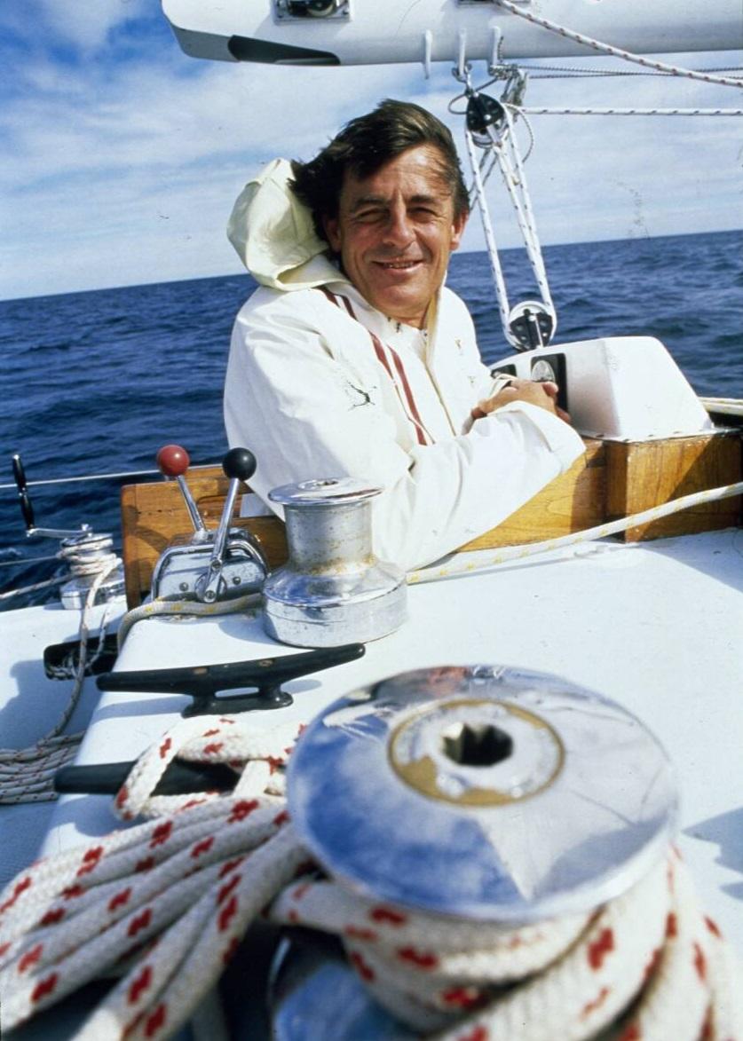 A close-up photo of Jon Sanders smiling with an arm resting on the boat. The ocean is calm behind him.