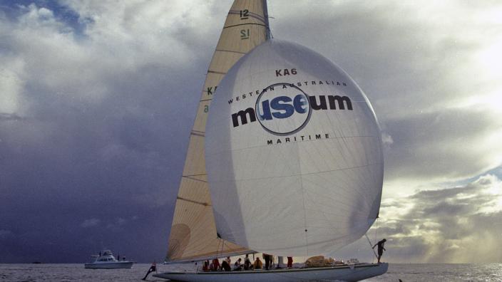 The Australia II sails the water, its sail showing a large logo of the Western Australian Maritime Museum.
