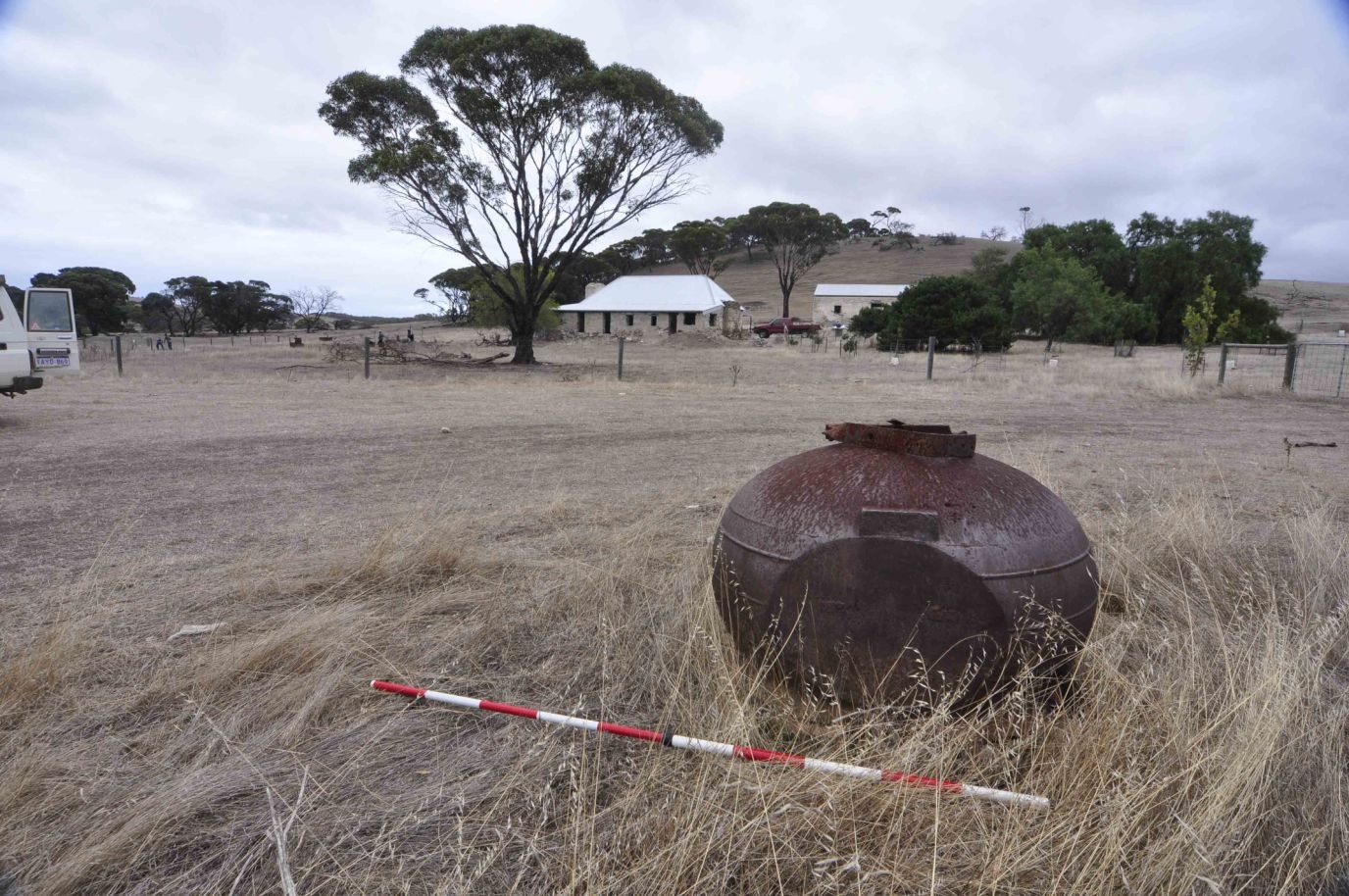 In an open grassy field sits a neglected, rusty large pot.