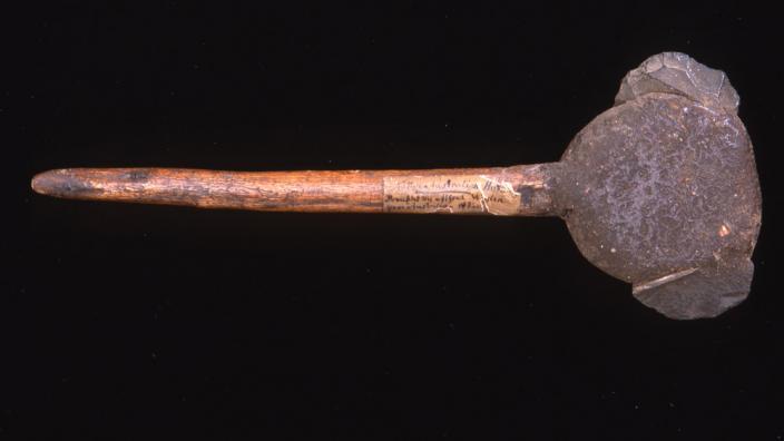 A tool with a thick wooden shaft and a very large stone head.