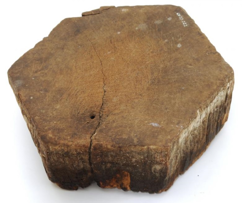 A six-sided thick wooden board with very worn edges. The underside of it is stained dark from laying on the ground for many years.