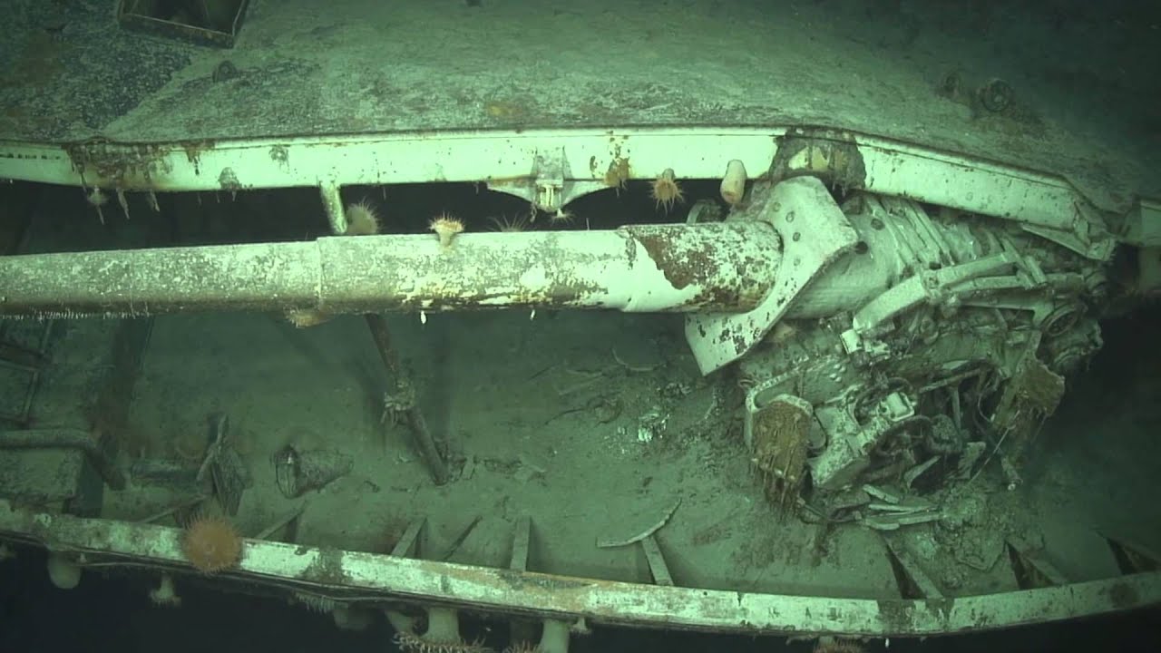 The long barrel of a ship's gun pokes out between the ship's bent and broken metal hull. A lot of the white paint is still visible.