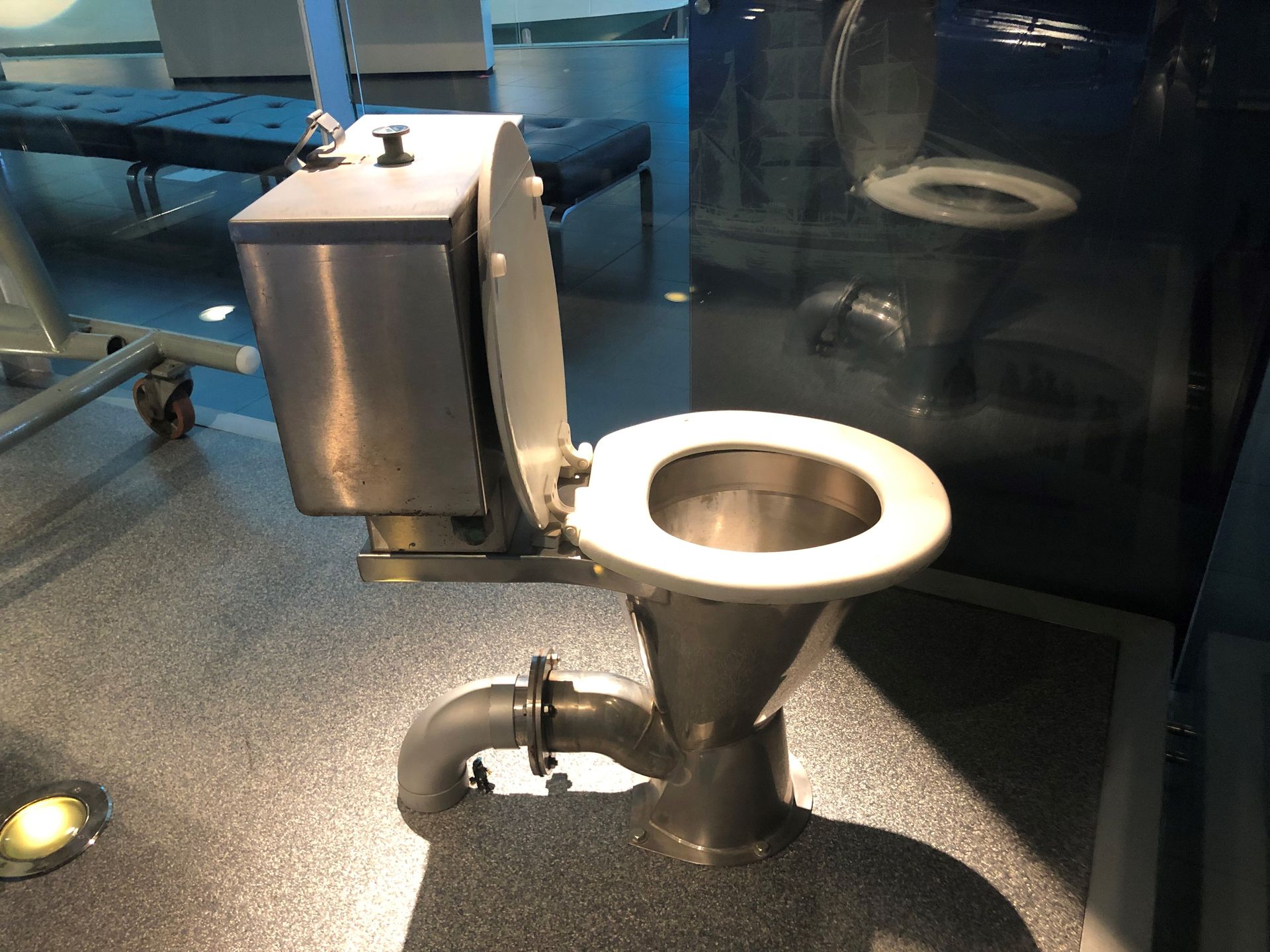 Behind a glass barrier is a metal toilet.
