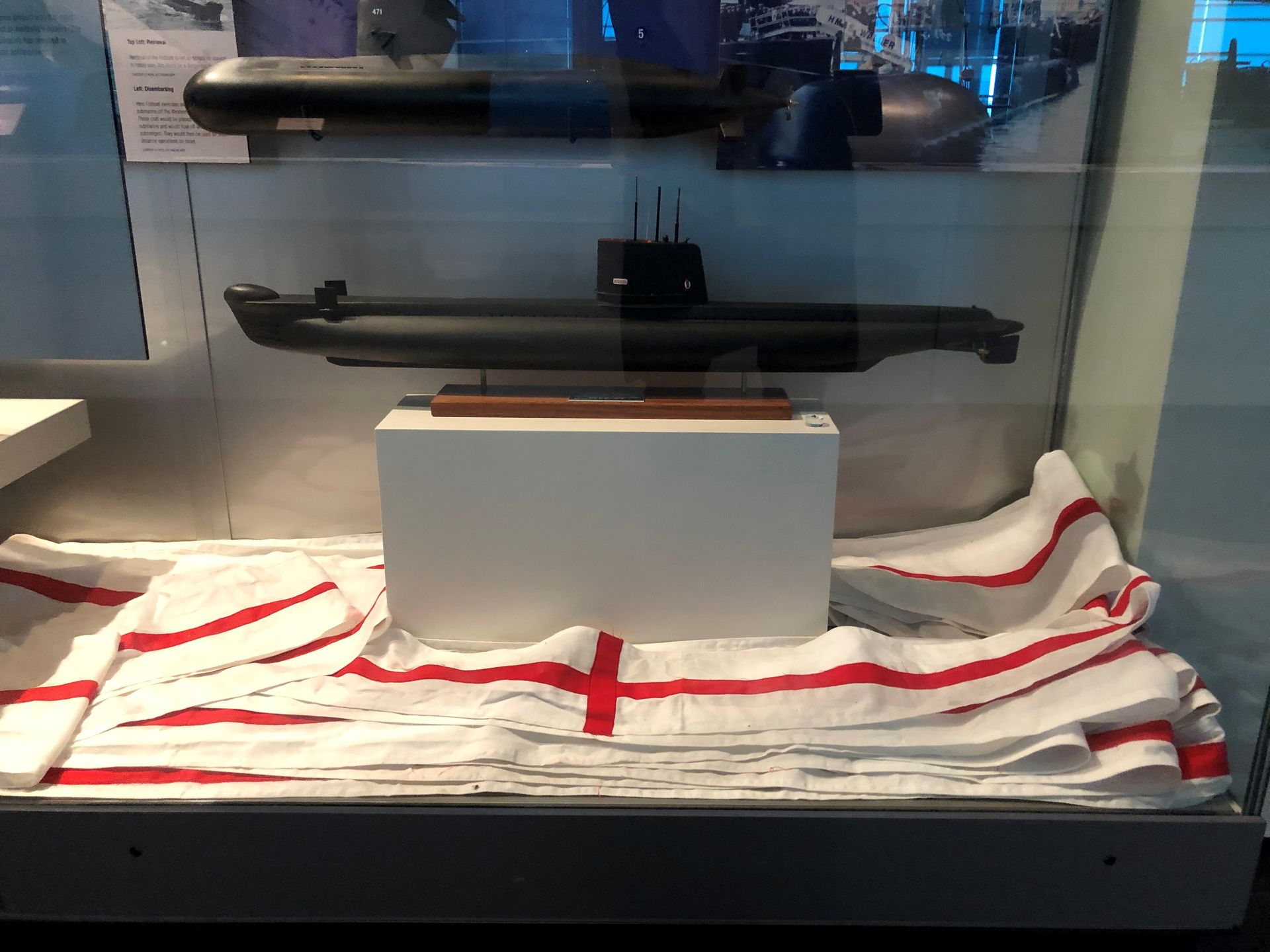 In a display case are some models of submarines, below them is a very long strip of white fabric with red stripes. This is the pennant.