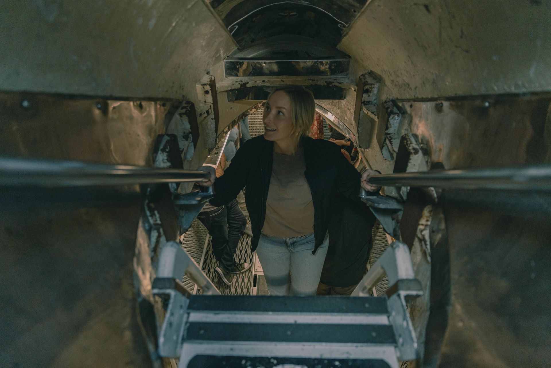 A smiling woman on the submarine tour descends a ladder down into the submarine.