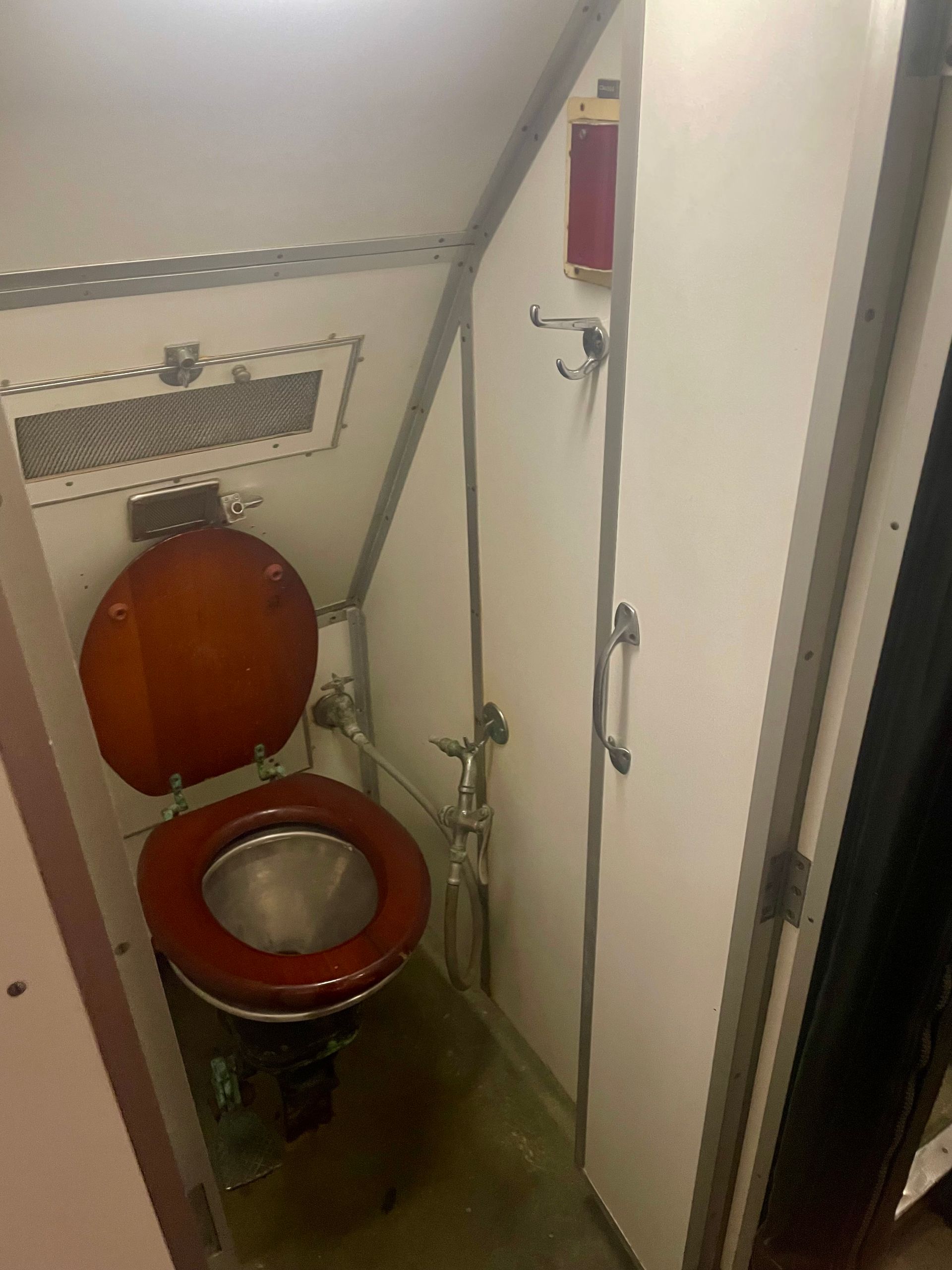 Toilet with wooden lid and seat in a tiny stall.