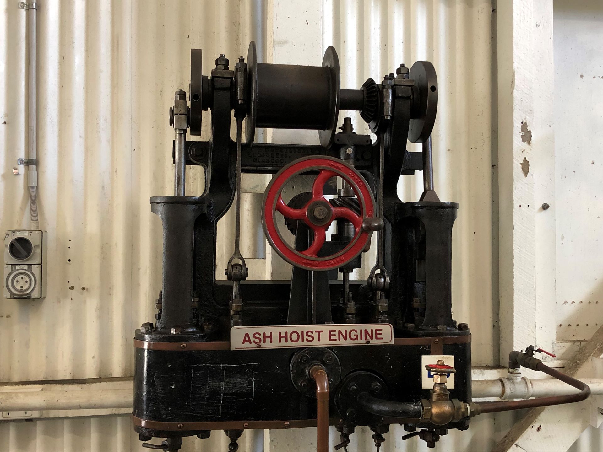 A green engine with a red wheel, mounted against the corrugated wall in the workshop.