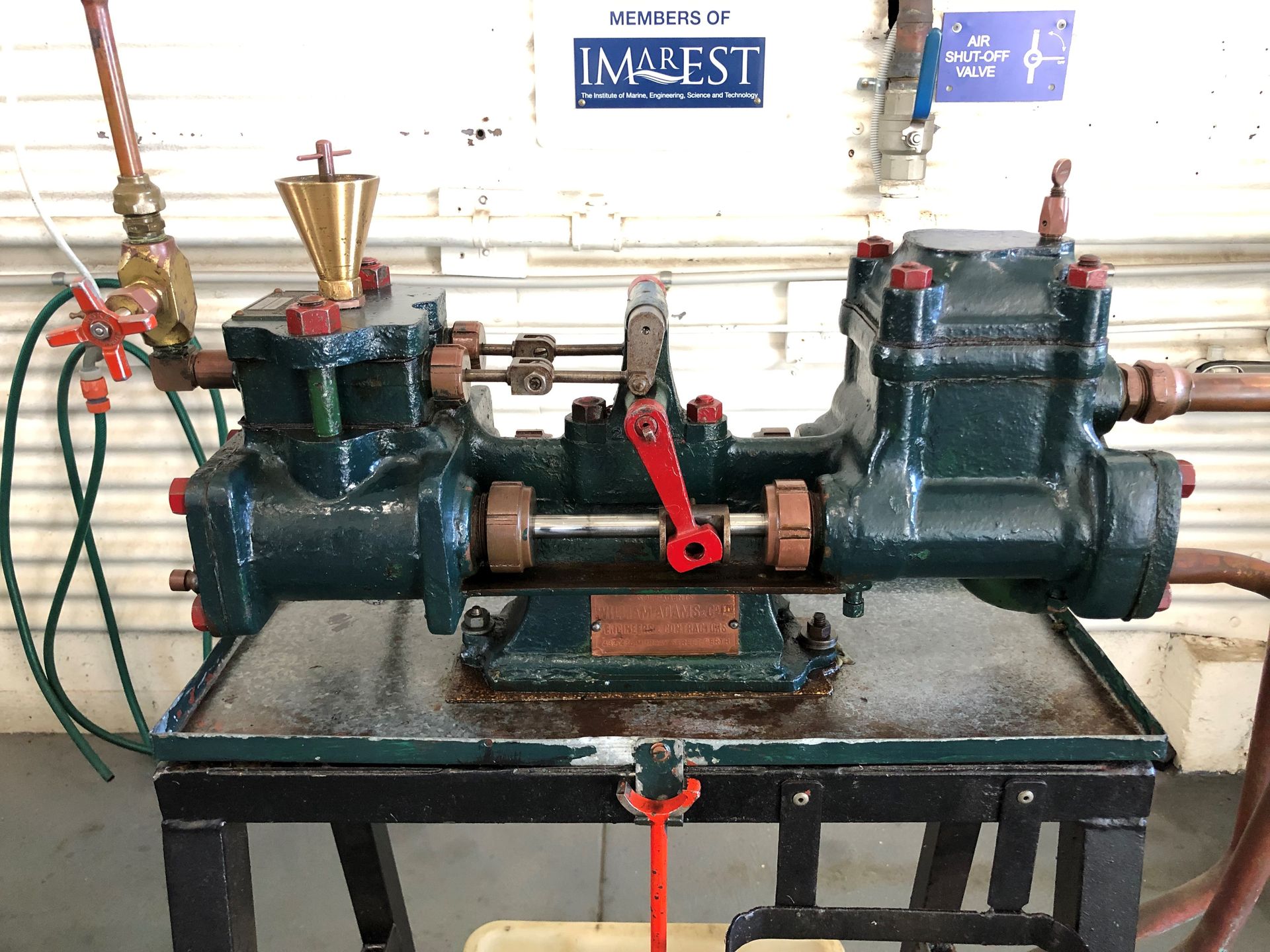 On top of a metal display sits a small green engine with some red painted parts.