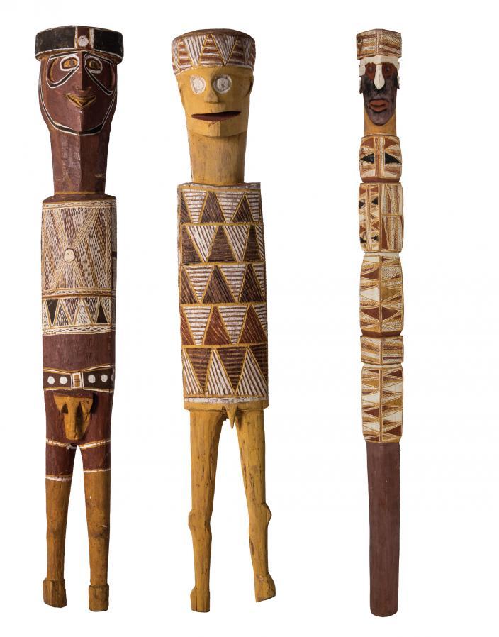 Three wooden carvings of people. Each has distinctive clothing and headwear.