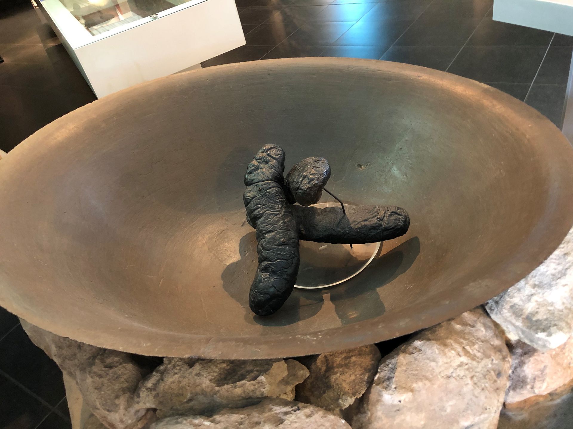 A large metal pan resting on stones. There are cooked sea slugs in the centre.