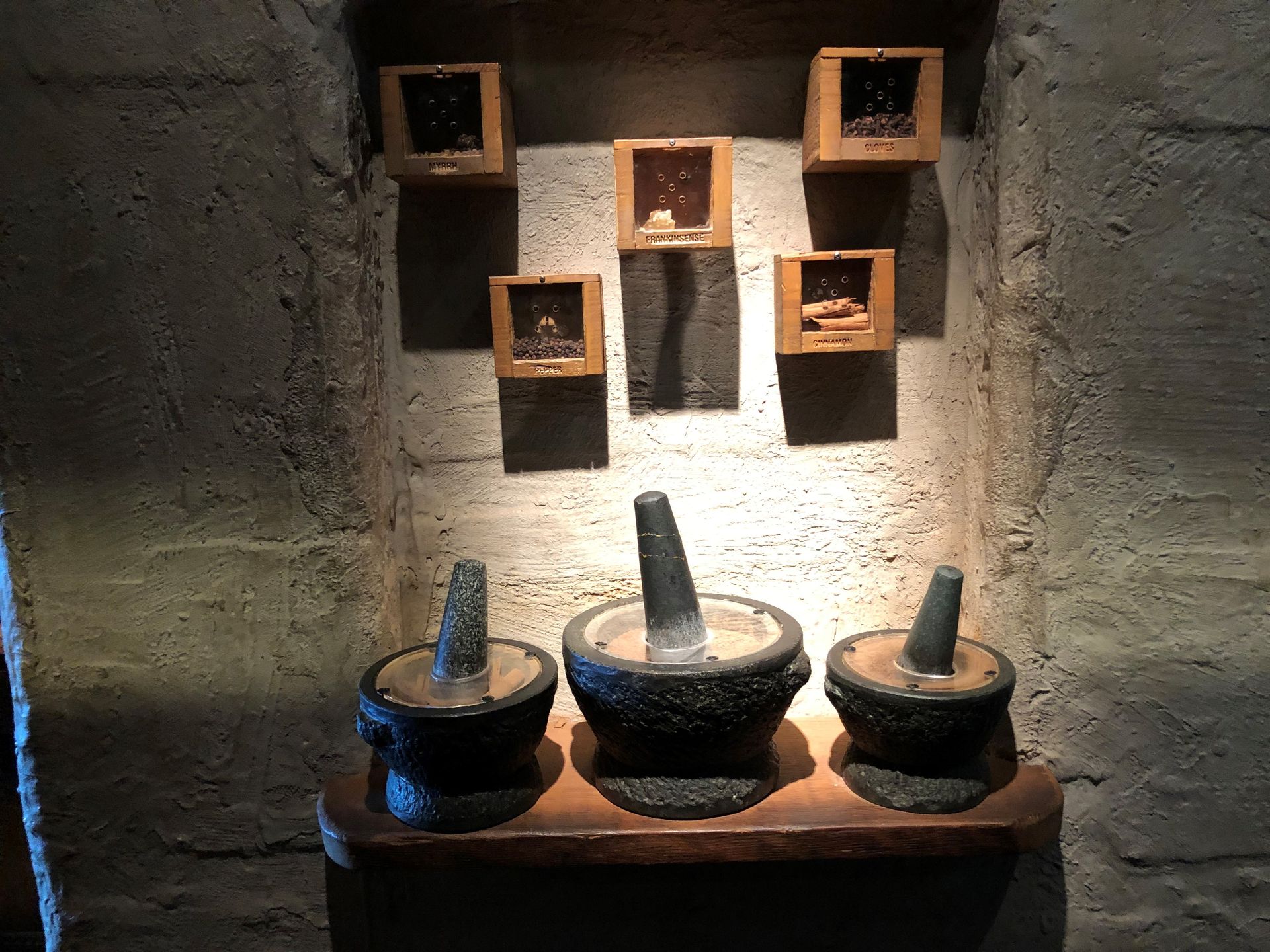 A display of three large spice grinding pestles, and spices in square boxes above.