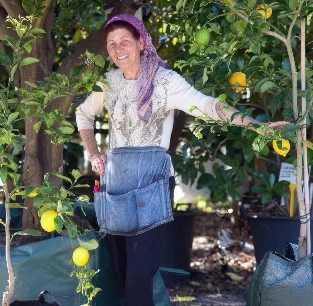 Lena in a work apron ad head scarf rests beside a lemon tree.