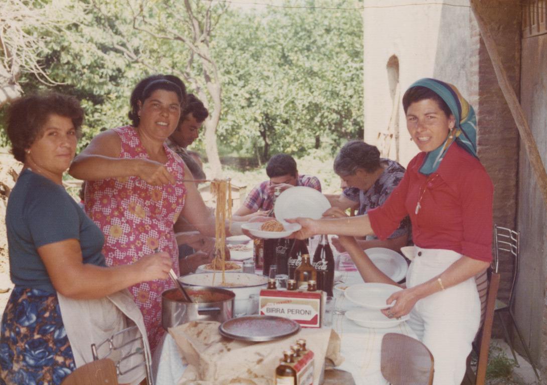A heap of spaghetti is being piled onto Lena's bowl. Bottles of Birra Peroni beer and Coco-Cola are on the table.