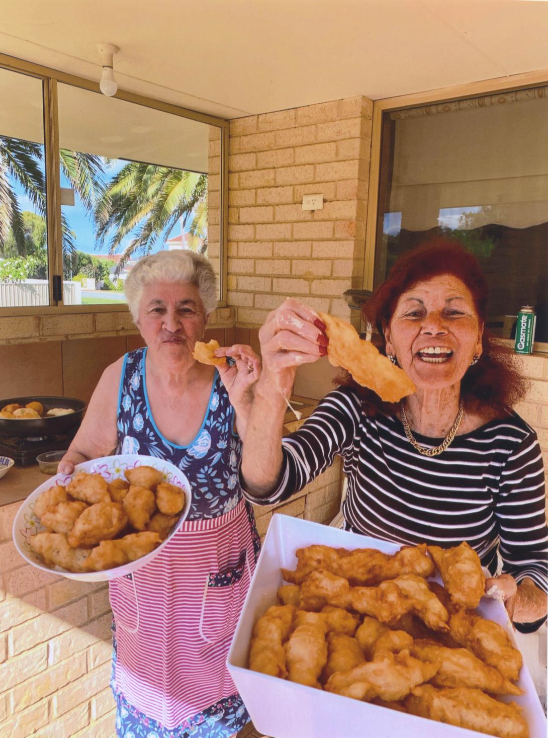 Lena and another woman holding up huge trays filled with food.