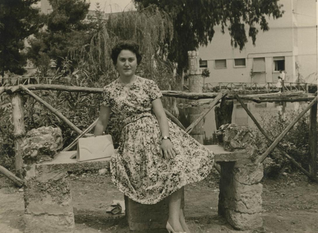 Giulia on a stone bench in front of a rustic wooden fence.
