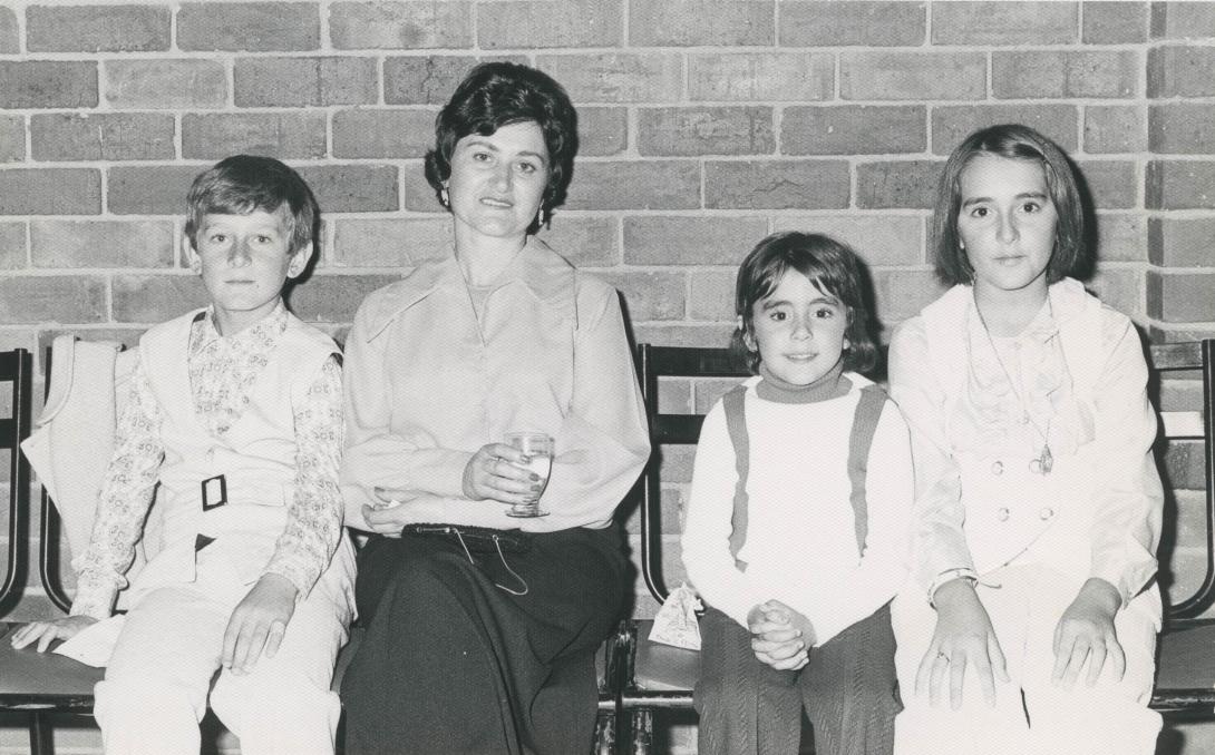 Giulia and three children seated against a brick wall.