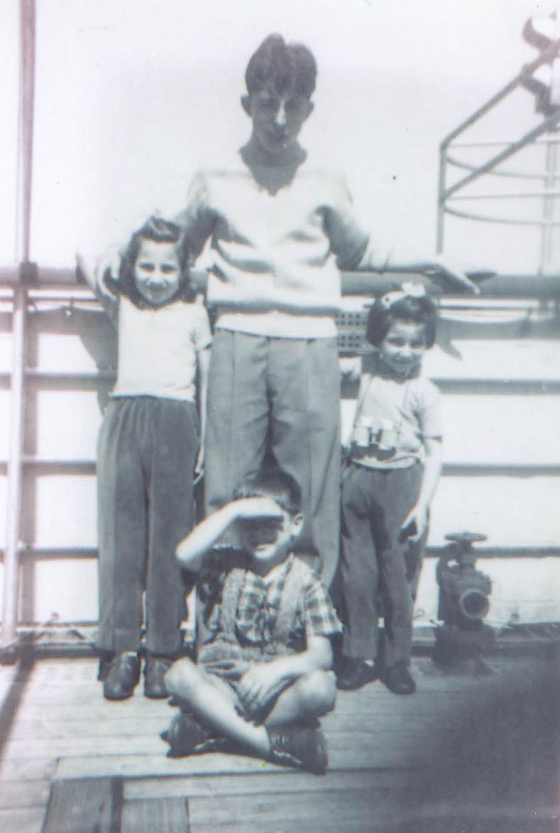 Four children squint from the bright sun at the railing of a passenger ship.