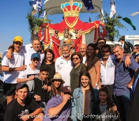Group of about 15 people gathered in front of a Madonna statue on a bright sunny day