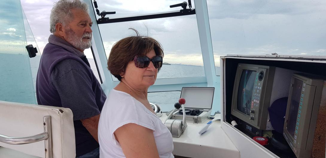 Land can be seen in the distance from the boat's cabin, where Anna and Jimmy look to the water.