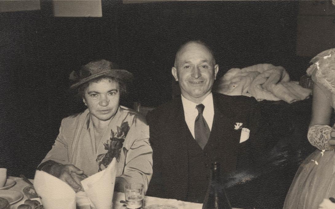 The well-dressed couple seated closely together at a table.