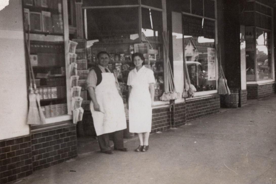 Anne smiles with a man in a white apron outside the store's front entrance.