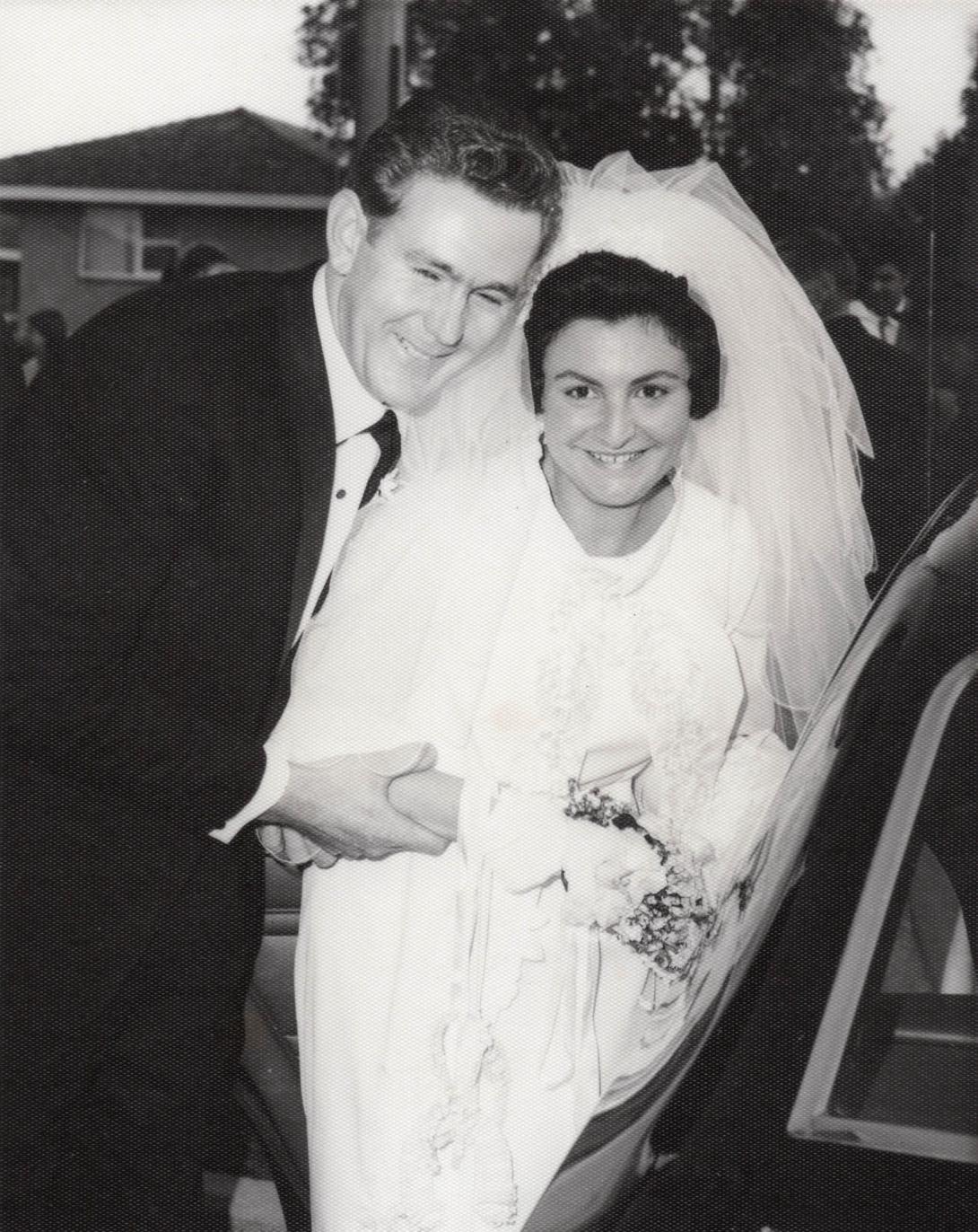 The couple smile as they bend down to enter their car.